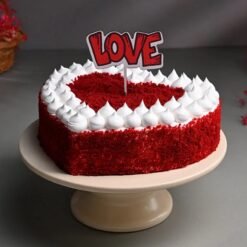 Heart-shaped red velvet cake with luscious cream cheese frosting and elegant red decorations.